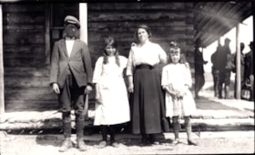 Family standing in front of a log building. (Images are provided for educational and research purposes only. Other use requires permission, please contact the Museum.) thumbnail