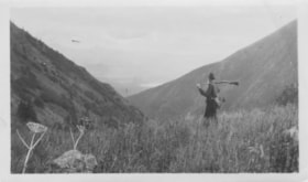 Man hiking above a valley holding a hunting rifle. (Images are provided for educational and research purposes only. Other use requires permission, please contact the Museum.) thumbnail