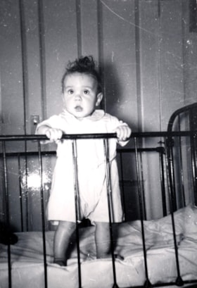 Unidentified baby standing in metal crib.. (Images are provided for educational and research purposes only. Other use requires permission, please contact the Museum.) thumbnail